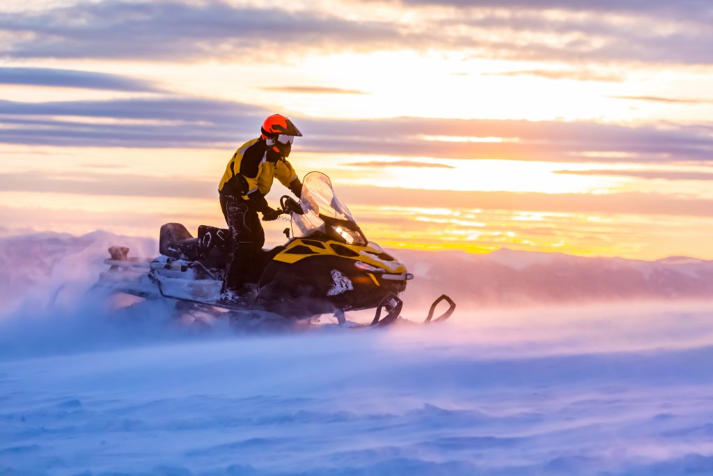 A man is riding a snowmobile in the mountains in the beautiful morning light.